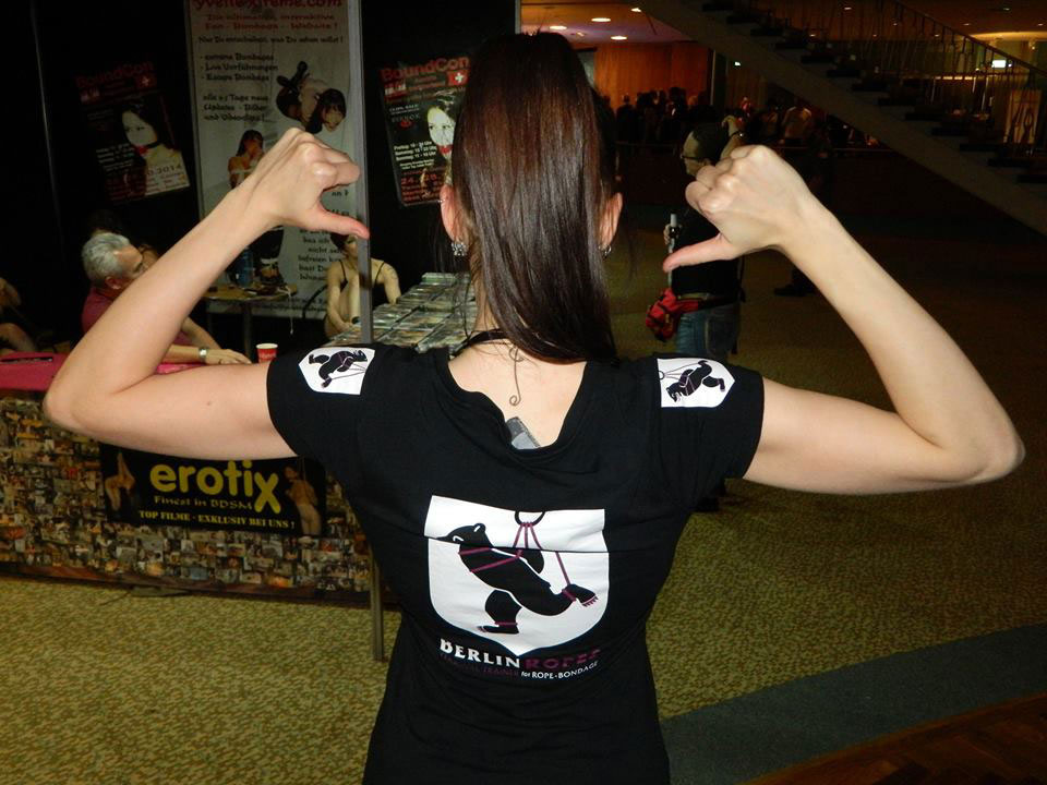 Der Rücken mit einem bedruckten Shirt. Die Daumen der Frau zeigen auf das Rückenmotiv