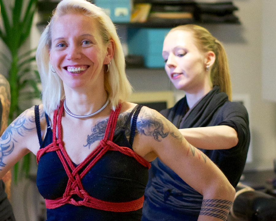 Eine lachende Frau, die gefesselt wird und einen roten Brustharness aus seilen trägt