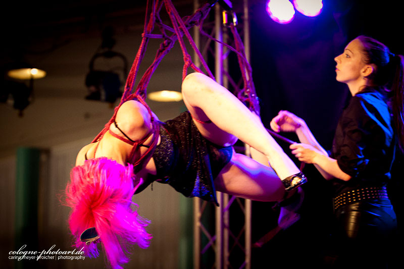 Eine Frau mit pinken Haaren hängt gefesselt auf einer Bühne