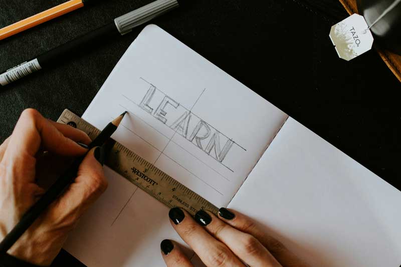Hände, die die Überschrift "Learn" mit Bleistift und Lineal unterstreichen. 