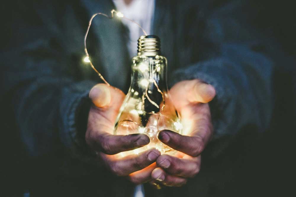 Zwei Hände die eine leuchtende Glühbirne festhalten