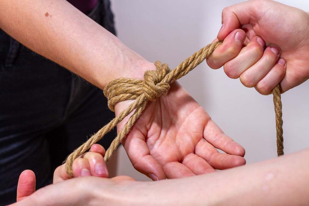 Eine einzelne Hand wird von zwei Händen gefesselt